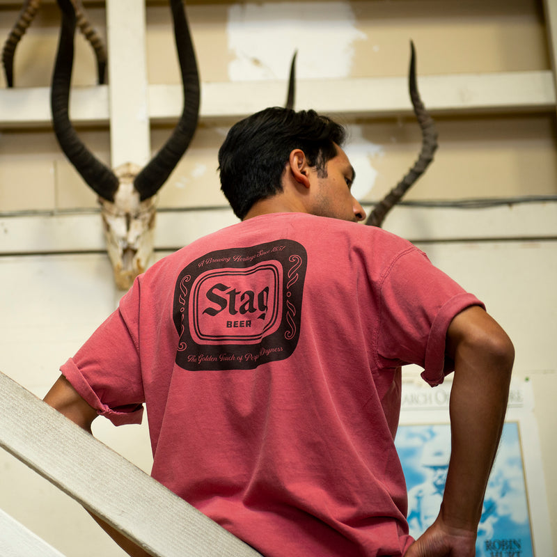 back of muted red t-shirt with black Stag Beer badge on a male model